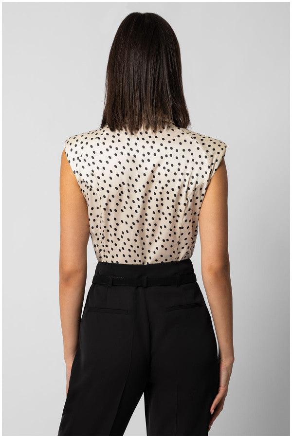 Back view of sleeveless satin elegant blouse with black polka dots paired with tailored black pants on model