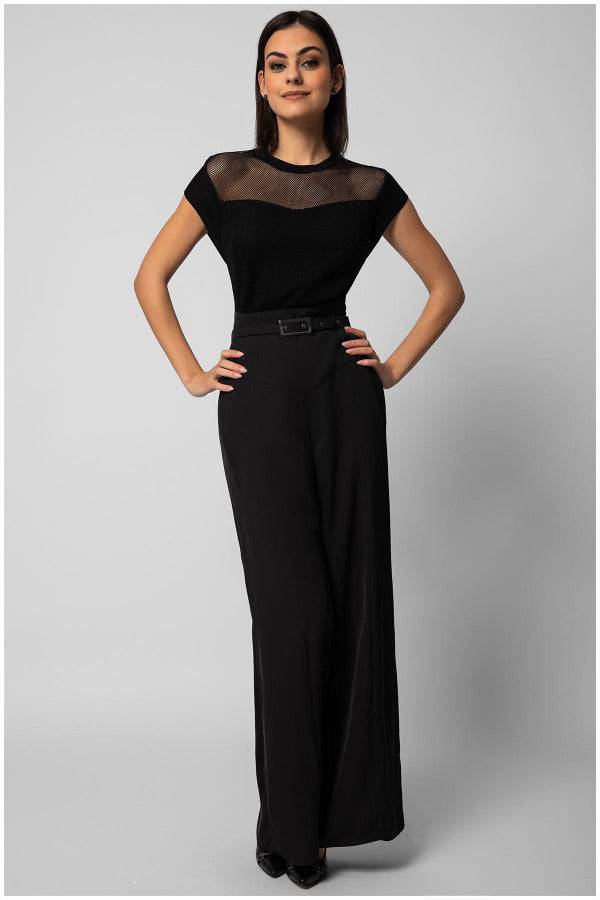 Woman wearing black Overall Aria jumpsuit with sheer panel neckline and wide-leg trousers, styled with a waist belt