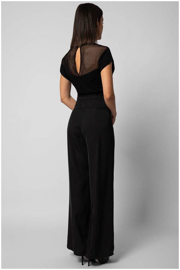Woman wearing black Aria Overall with sheer back panel and wide-leg pants viewed from behind