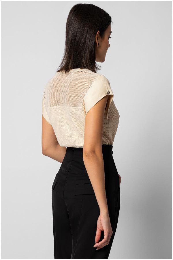 Woman wearing cream short sleeve blouse with sheer panel and black trousers standing sideways against gray background womens short sleeve tops