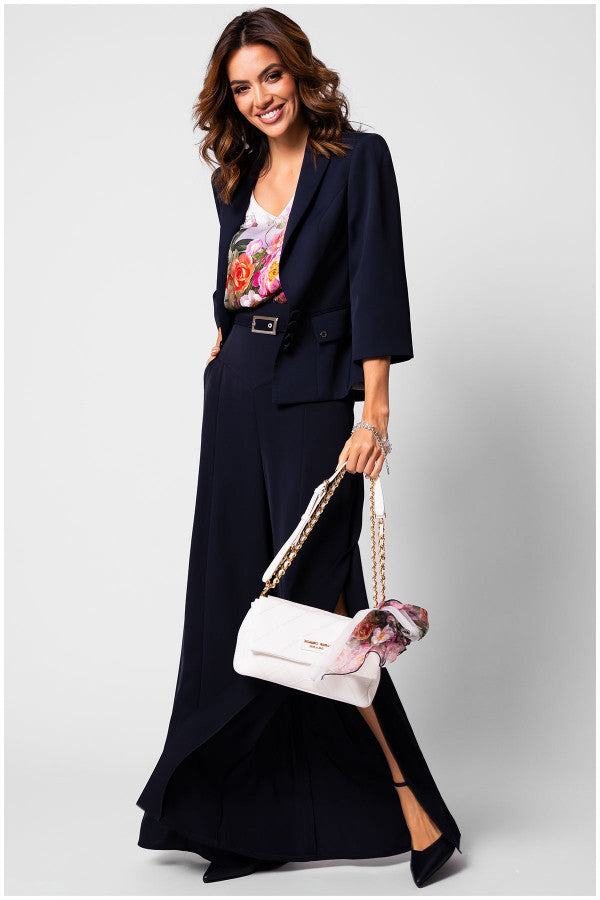 Woman wearing navy tailored blazer Alexa blazer with floral top and wide-leg trousers, holding white handbag with scarf detail
