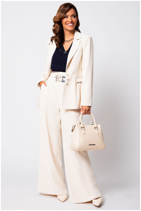 Woman in an ivory Luna Fashion House suit holding a beige handbag against a light gray background