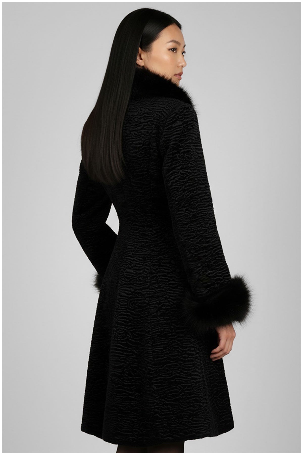 Woman wearing a black textured coat with fur trim on a gray background