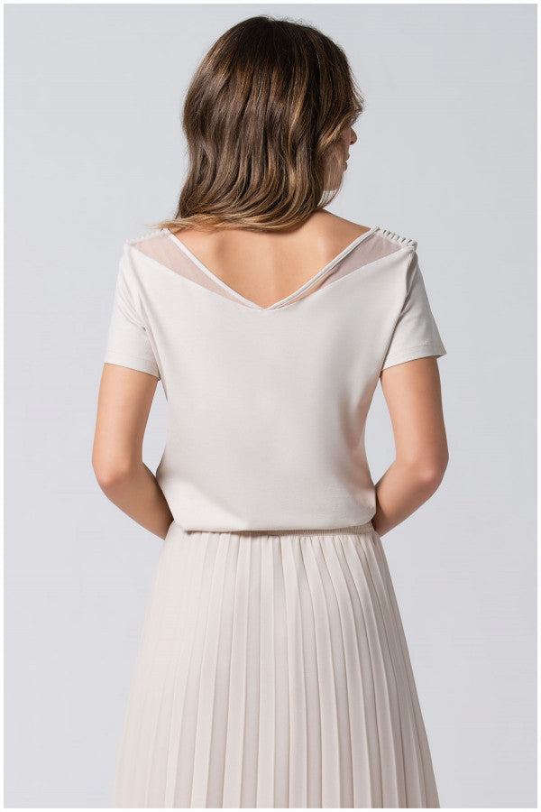 Woman wearing ivory Lola business Top with pleated neckline and short sleeves, paired with a pleated skirt, shown from the back