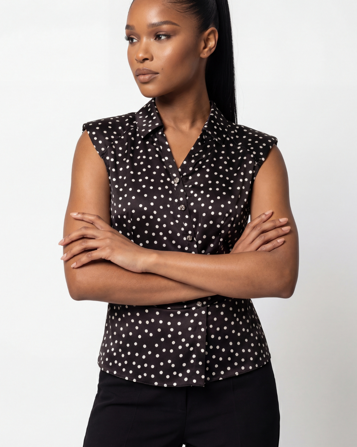 Black polka dot satin sleeveless V-neck blouse with diagonal button detail on a neutral studio background