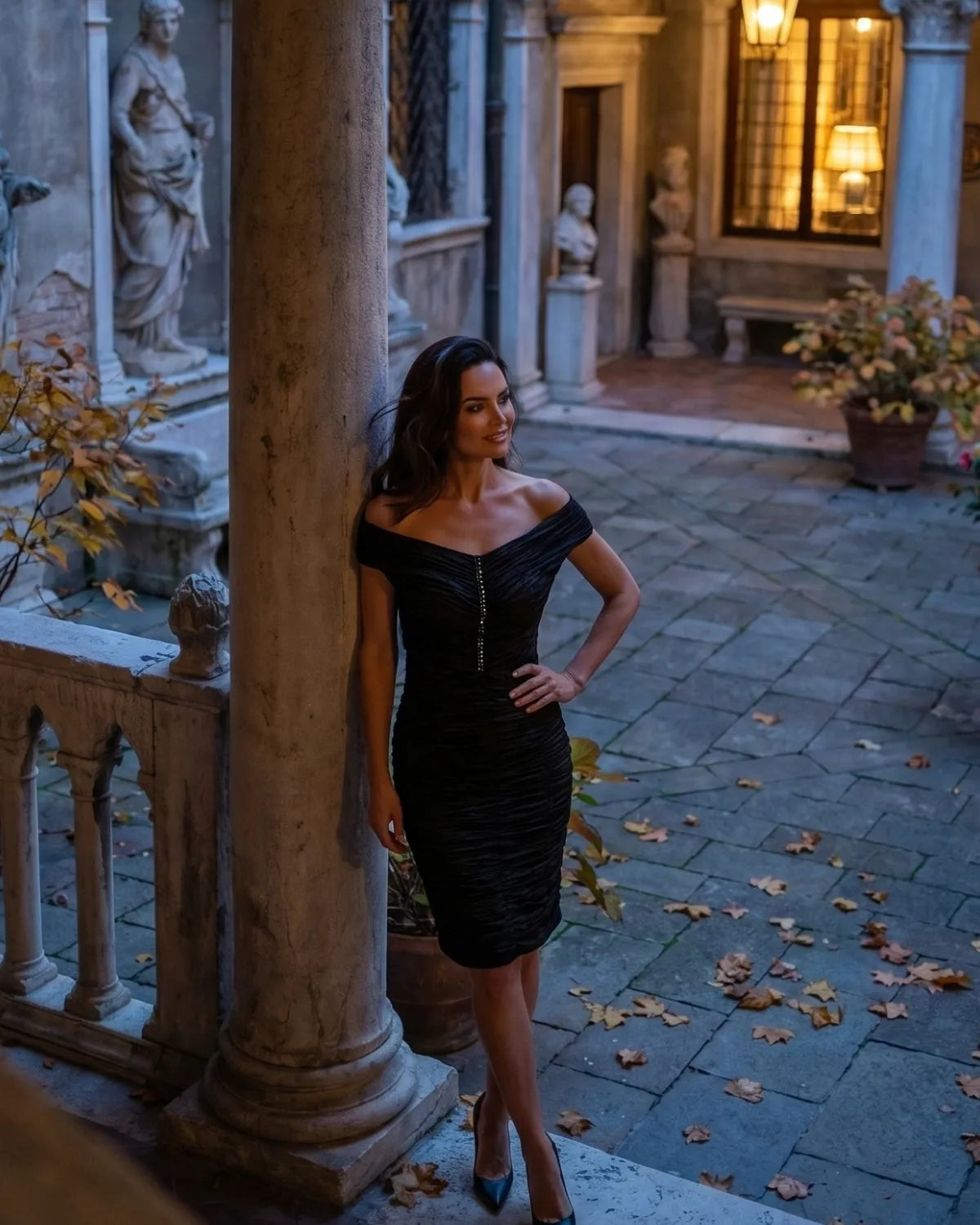 Black off shoulder ruched dress just below the knee, under a stone arch at night