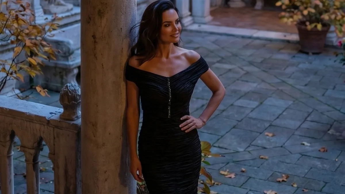 Black off shoulder ruched dress just below the knee, under a stone arch at night
