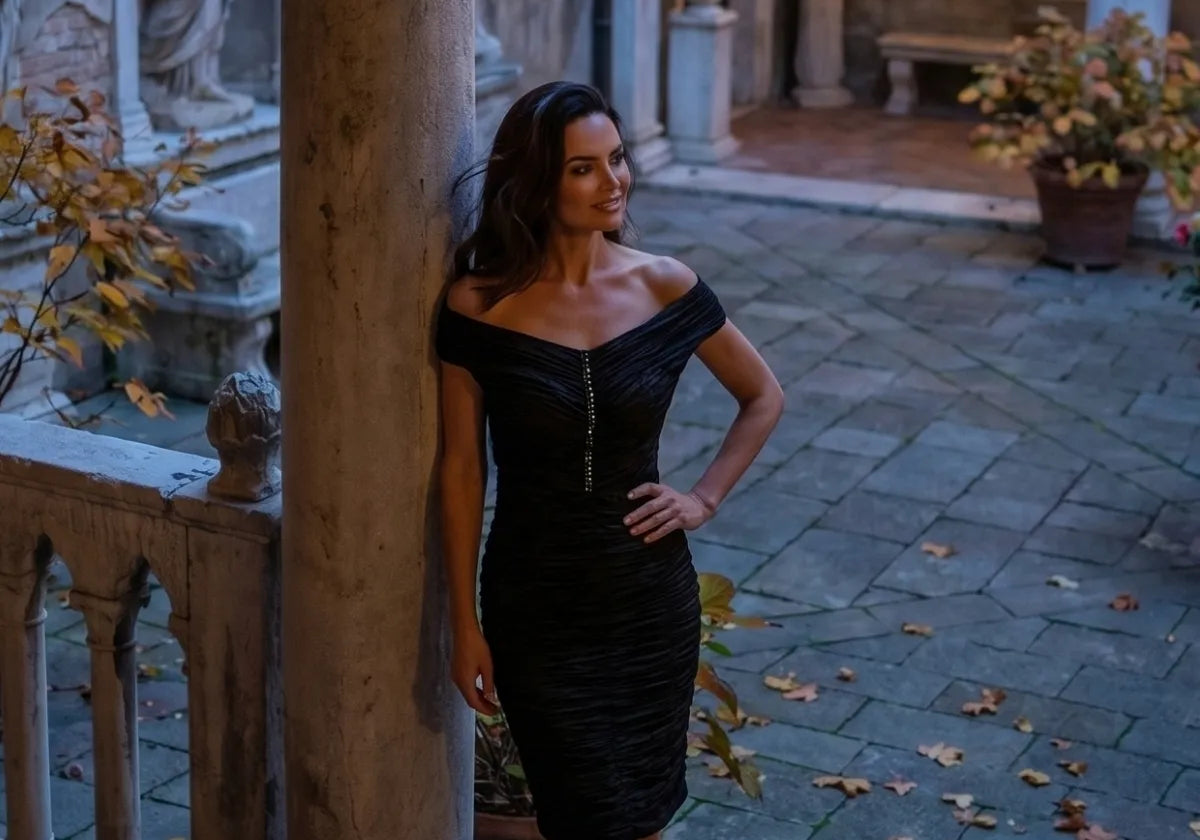 Black off shoulder ruched dress just below the knee, under a stone arch at night