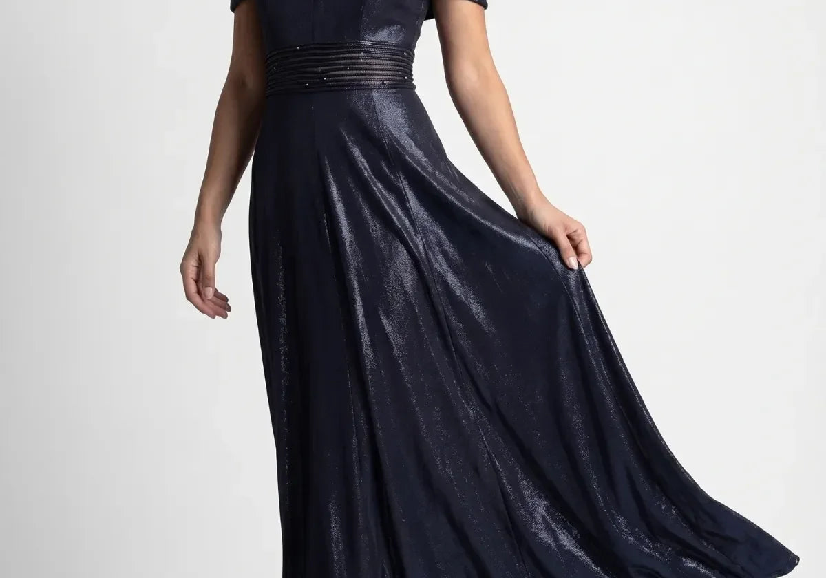 Deep navy off-shoulder maxi gown with pleated neckline, beaded waist and flowing skirt on a formal evening setting