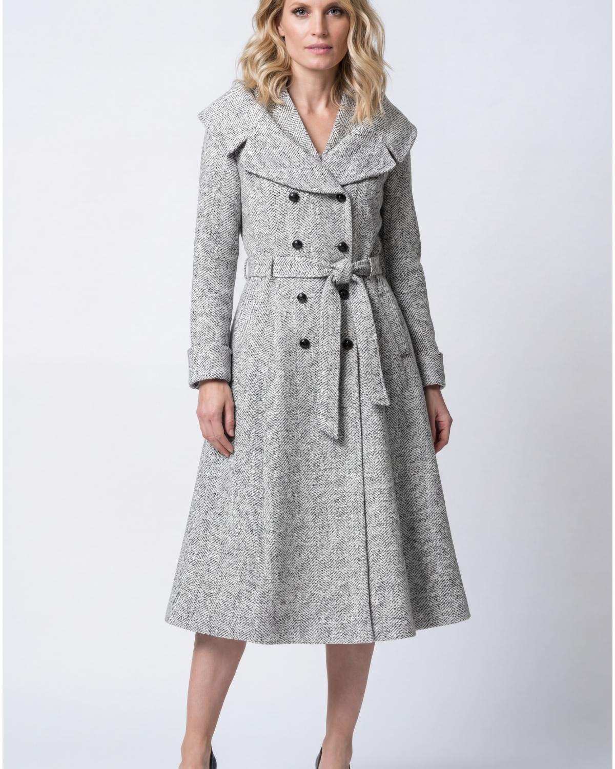 A selection of handmade Luna Fashion House occasion dresses and coats including the Nicole wool wrap coat in gray herringbone and the Emma teal floral jacquard light coat displayed in a European atelier setting