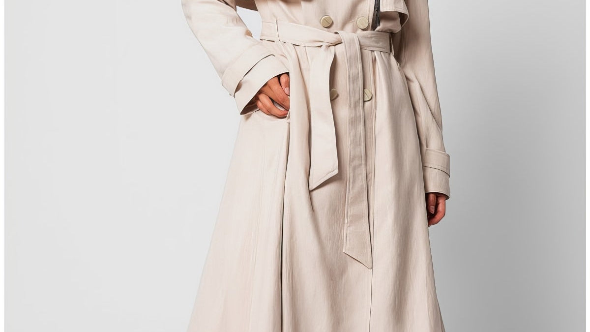 Beige classic long coat with self-fabric belt and full lining worn over ivory wide-leg trousers, transitional season