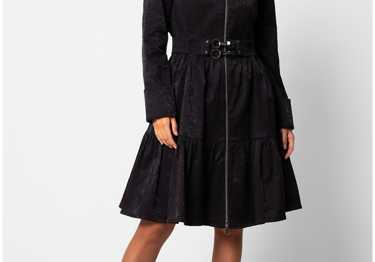 Black Cotton Short Tailored Coat, Iris, on the model: a knee-length black coat with a wide stand-up collar, a front zip, a wide belt with a double-ring buckle, and a tiered flared hem
