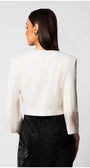 Woman wearing a white tailored blazer jacket with structured shoulders and a round neckline, viewed from the back.