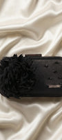 Black evening clutch with feather flower and beadwork styled on cream satin