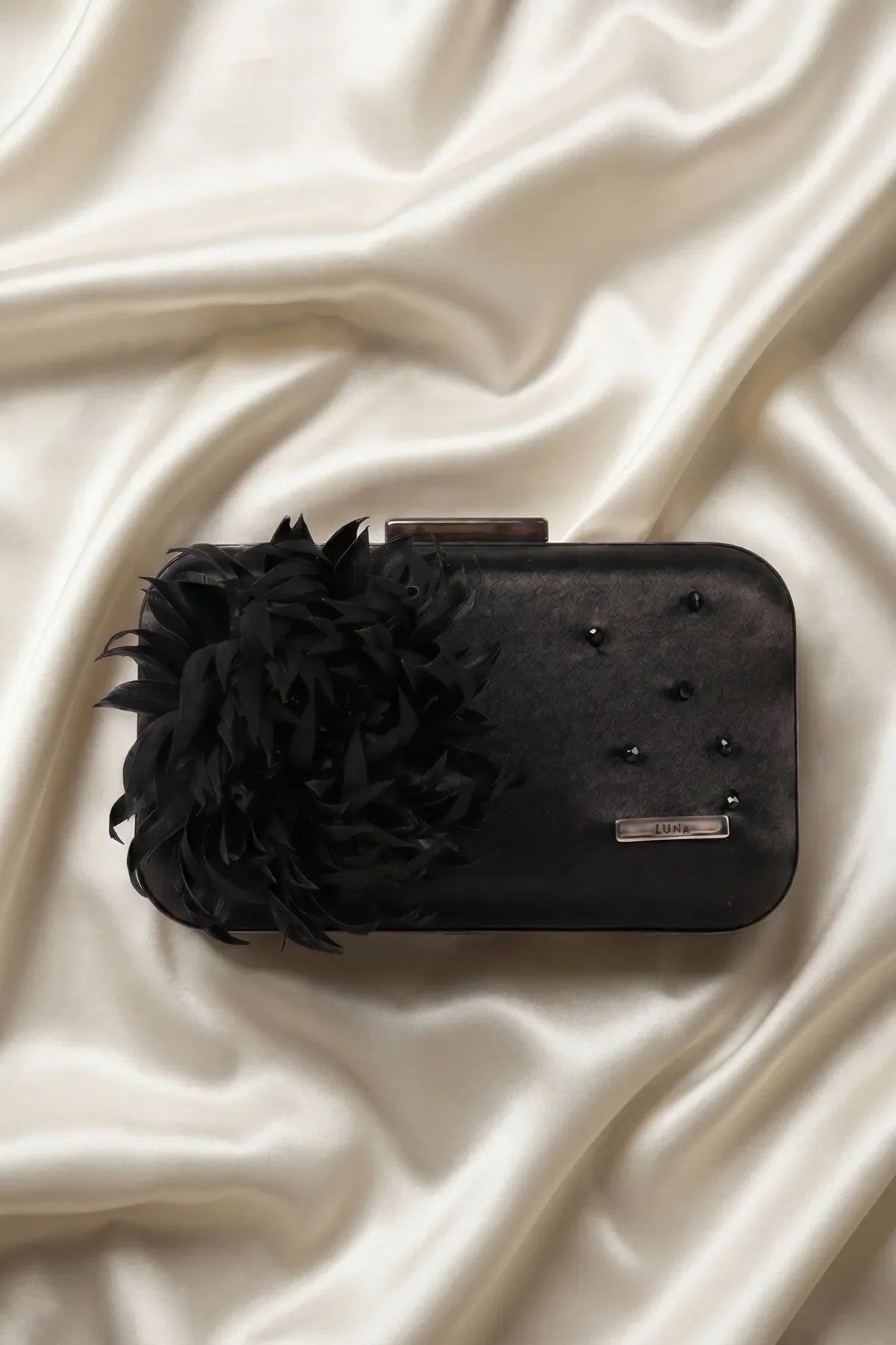 Black evening clutch with feather flower and beadwork styled on cream satin