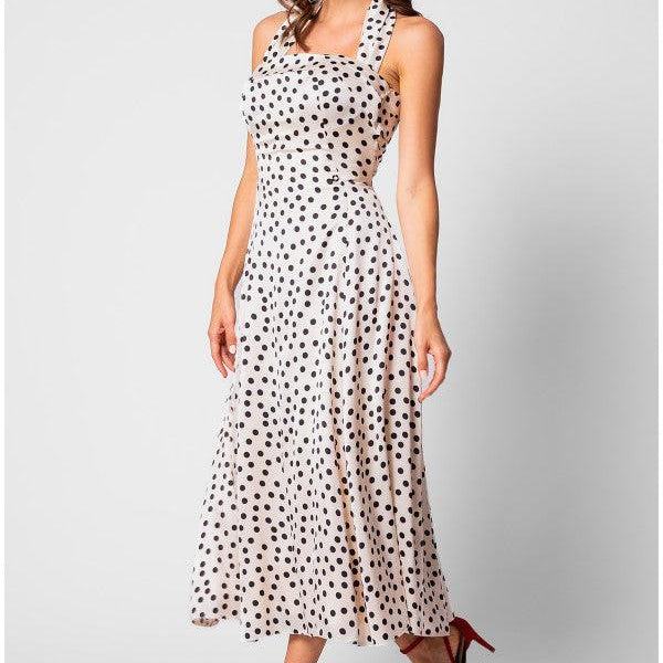 Woman wearing a white elegant midi dress satin dress with black polka dots and red heels, smiling against a plain background.