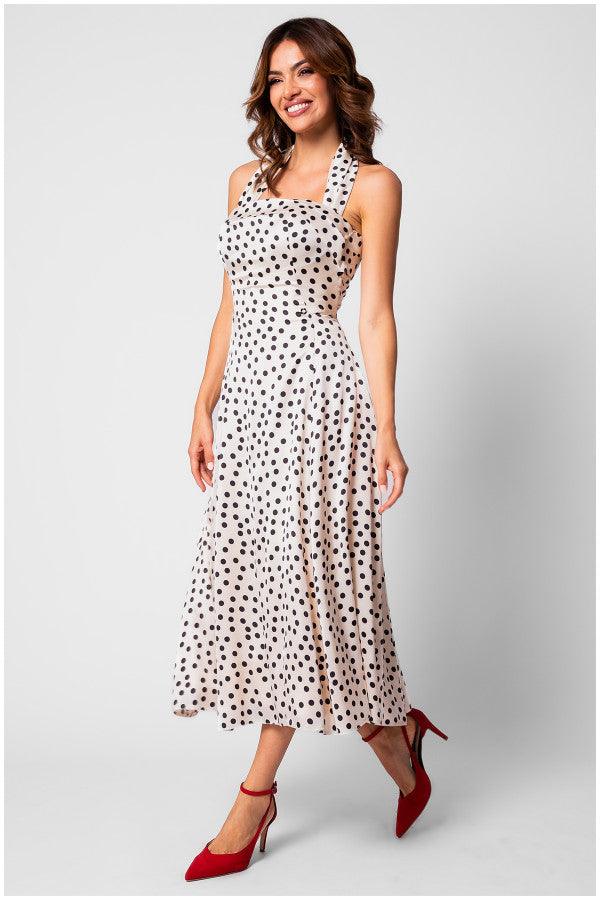 Woman wearing a white elegant midi dress satin dress with black polka dots and red heels, smiling against a plain background.