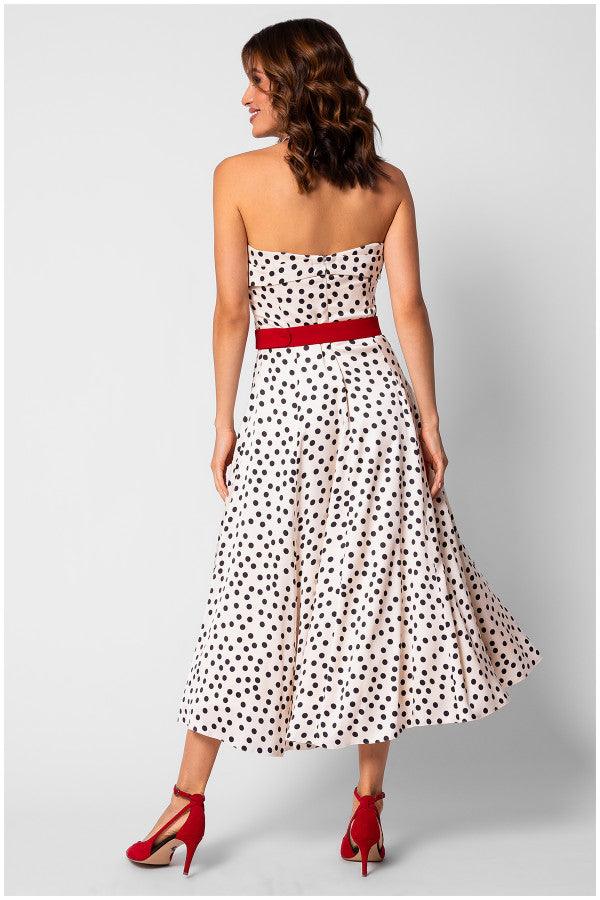 Back view of a strapless white elegant midi dress with black polka dots, red belt, and red high heel shoes