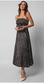Woman wearing a black elegant midi dress satin strapless midi dress with white polka dots and beige heels holding a small clutch bag.
