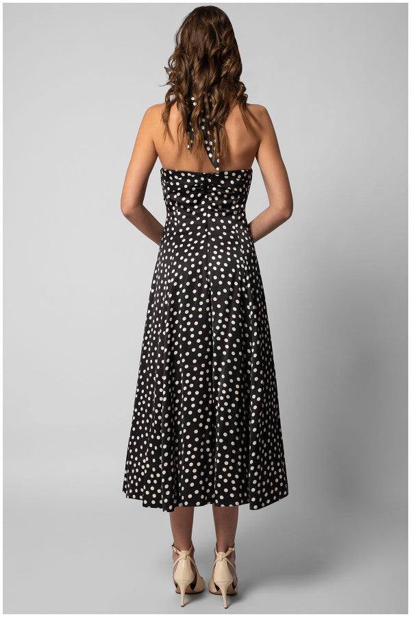 Back view of strapless black elegant midi dress satin midi dress with white polka dots and flowing multi-layered skirt on model.