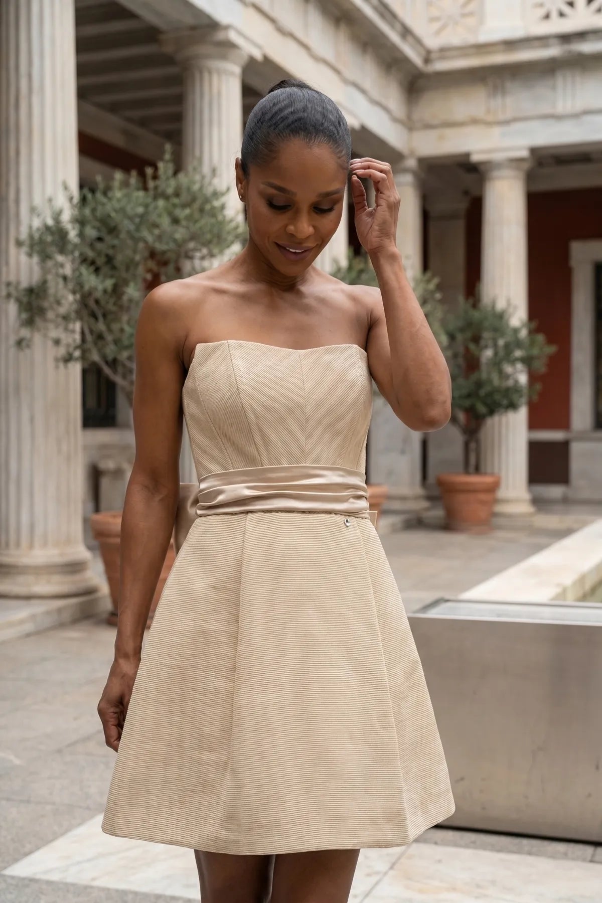 Melisa beige strapless mini corset dress with flared skirt in a refined courtyard setting.