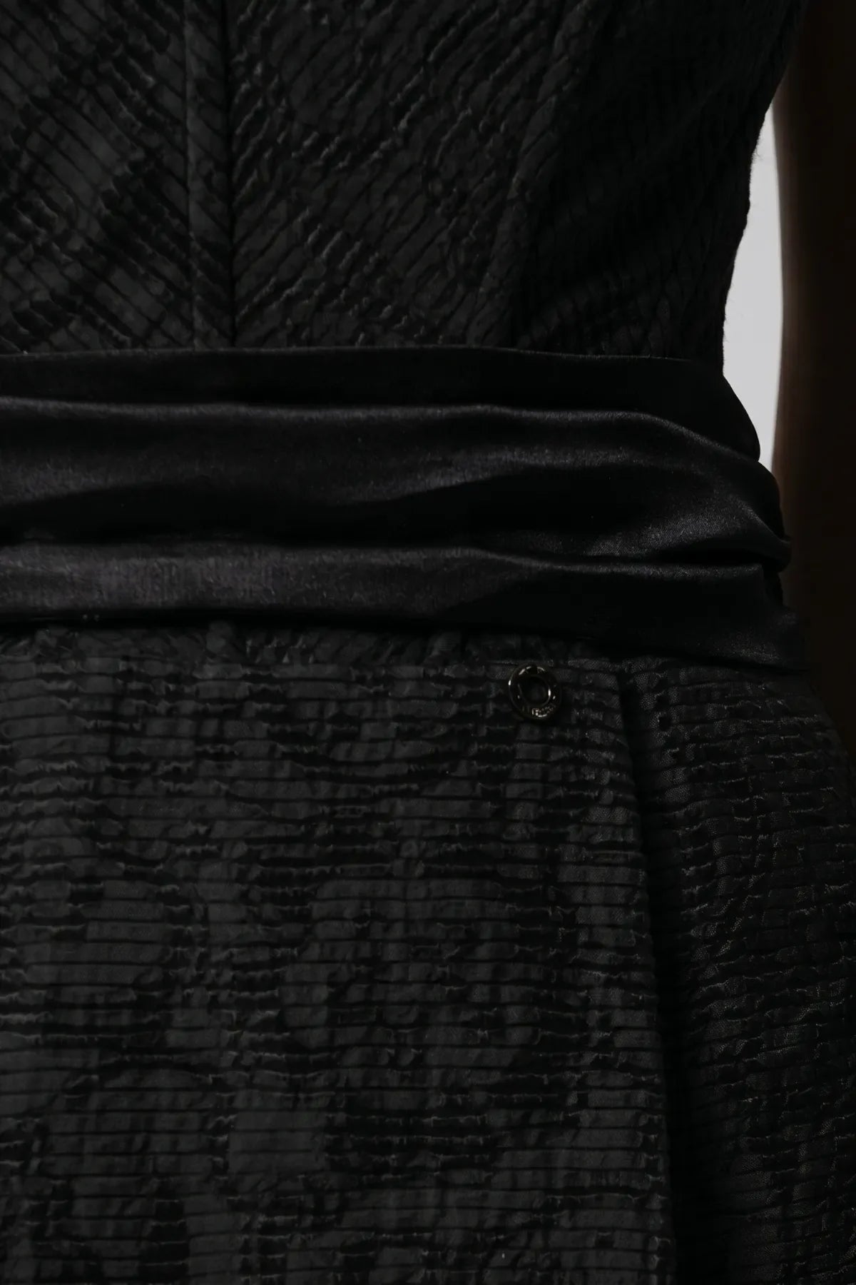 Fabric close-up of Melisa black mini dress showing textured weave, satin waistband, and Luna accent.