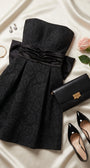 Melisa black strapless mini dress styled on cream satin with black heels, clutch, jewelry, and a rose.
