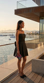 Melisa black strapless mini dress styled on a marina balcony with heels and a floral clutch.