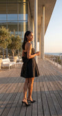 Melisa black strapless mini dress worn on a seaside terrace with the oversized back bow visible.