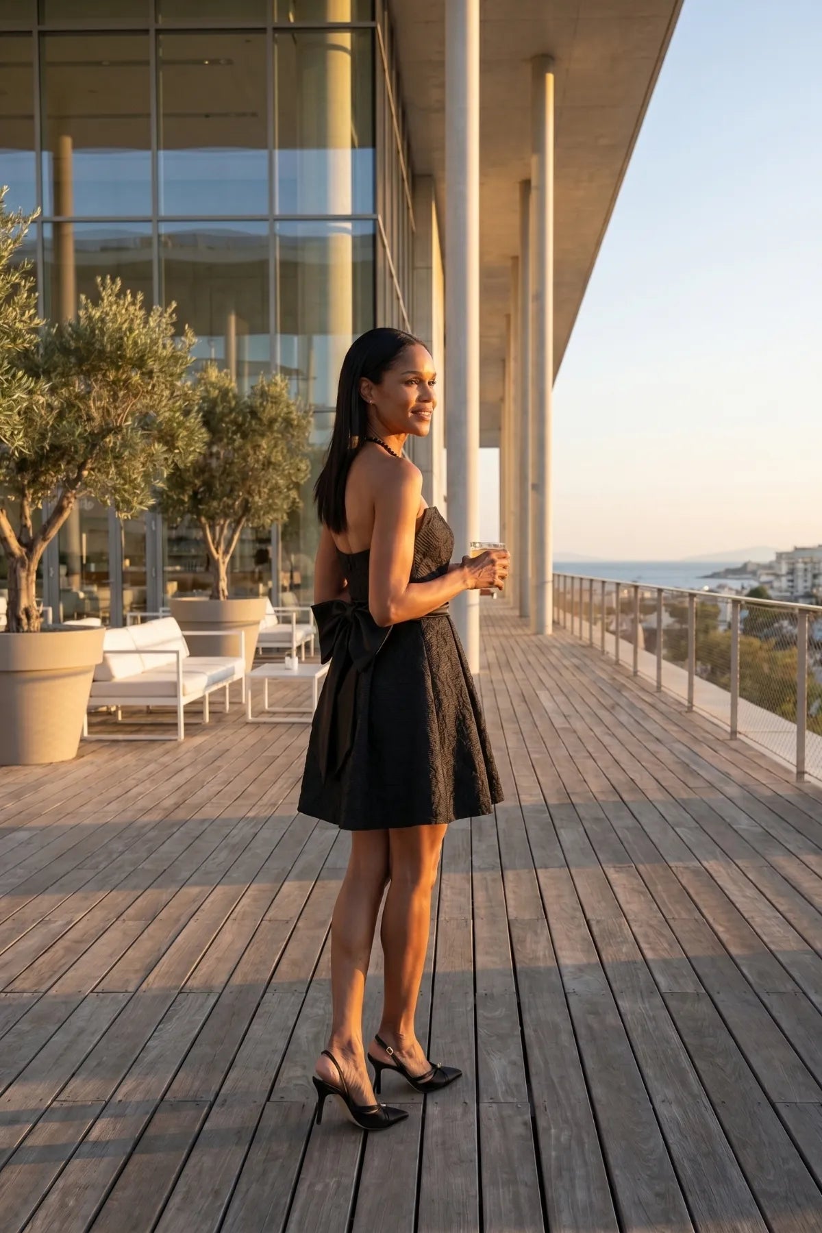 Melisa black strapless mini dress worn on a seaside terrace with the oversized back bow visible.