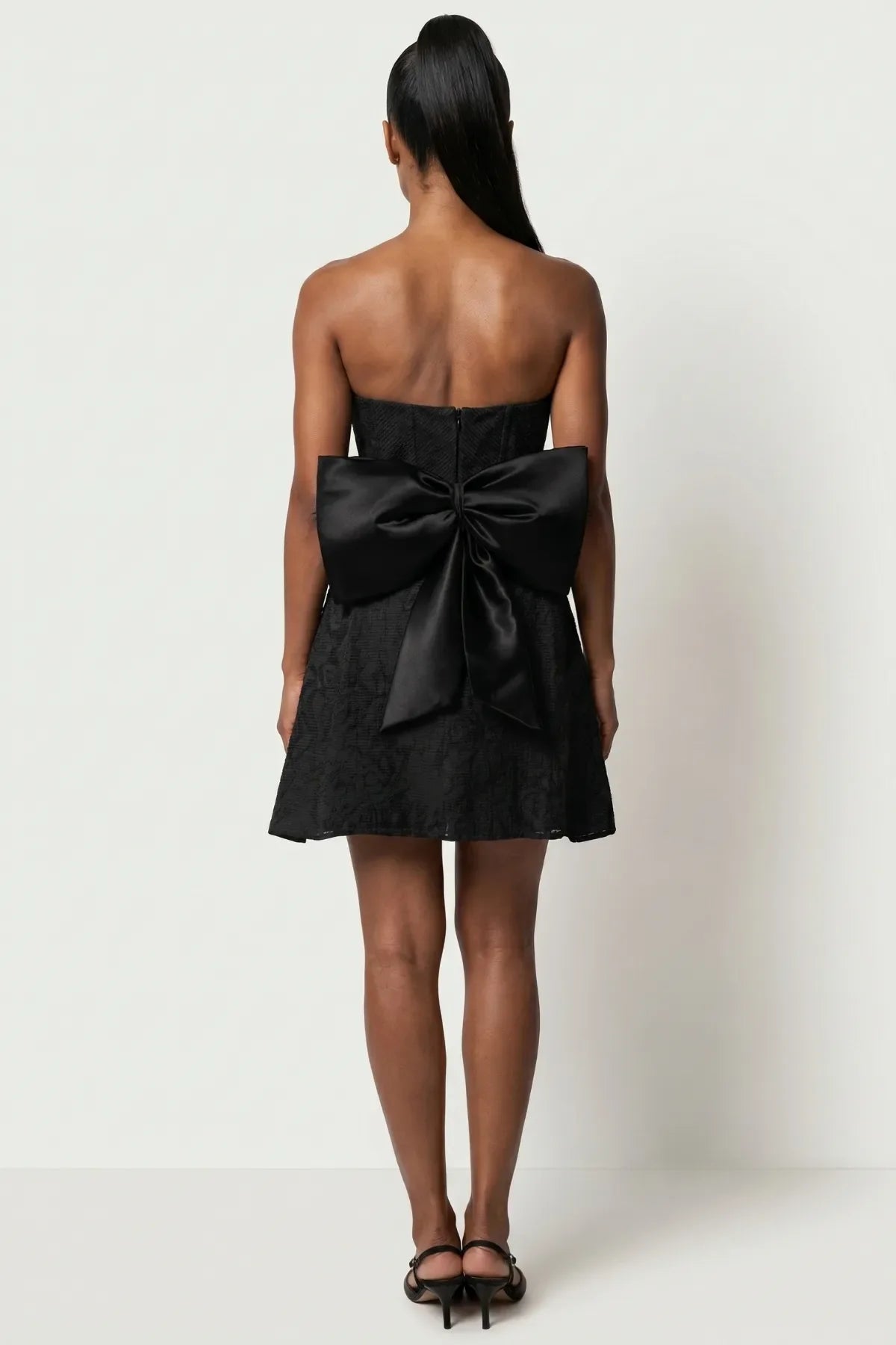 Back view of Melisa black mini dress with oversized removable bow, center zipper, and flared skirt.
