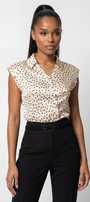 Woman wearing a sleeveless polka dot blouse and black pants on a white background