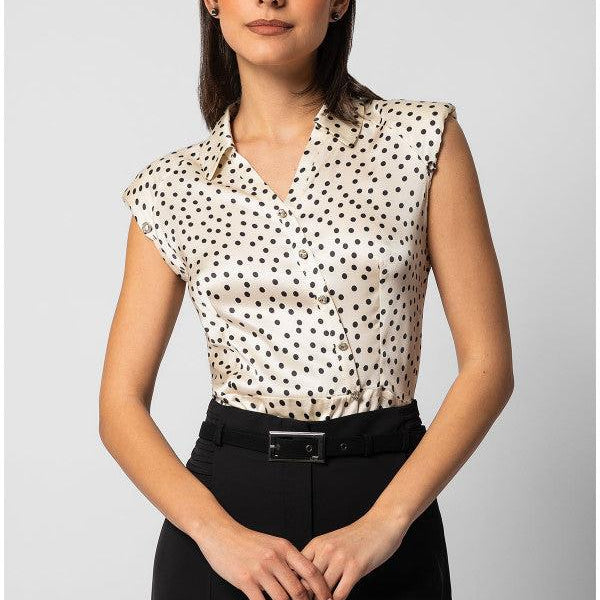 Woman wearing sleeveless satin elegant blouse with black polka dots and decorative buttons paired with black tailored pants