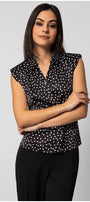 Woman wearing a sleeveless black satin elegant blouse with white polka dots and decorative diagonal buttons, styled professionally.