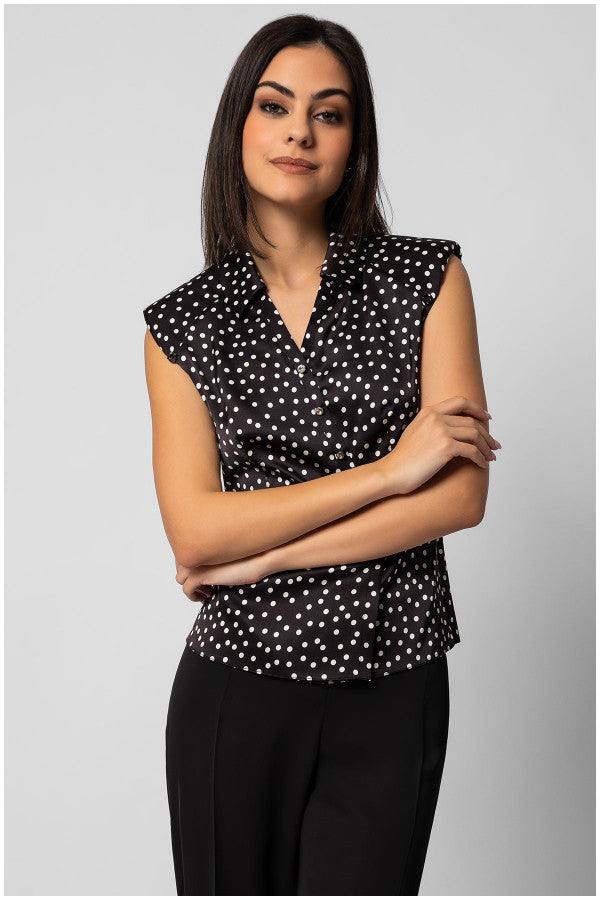 Woman wearing a sleeveless black satin elegant blouse with white polka dots and decorative diagonal buttons, styled professionally.