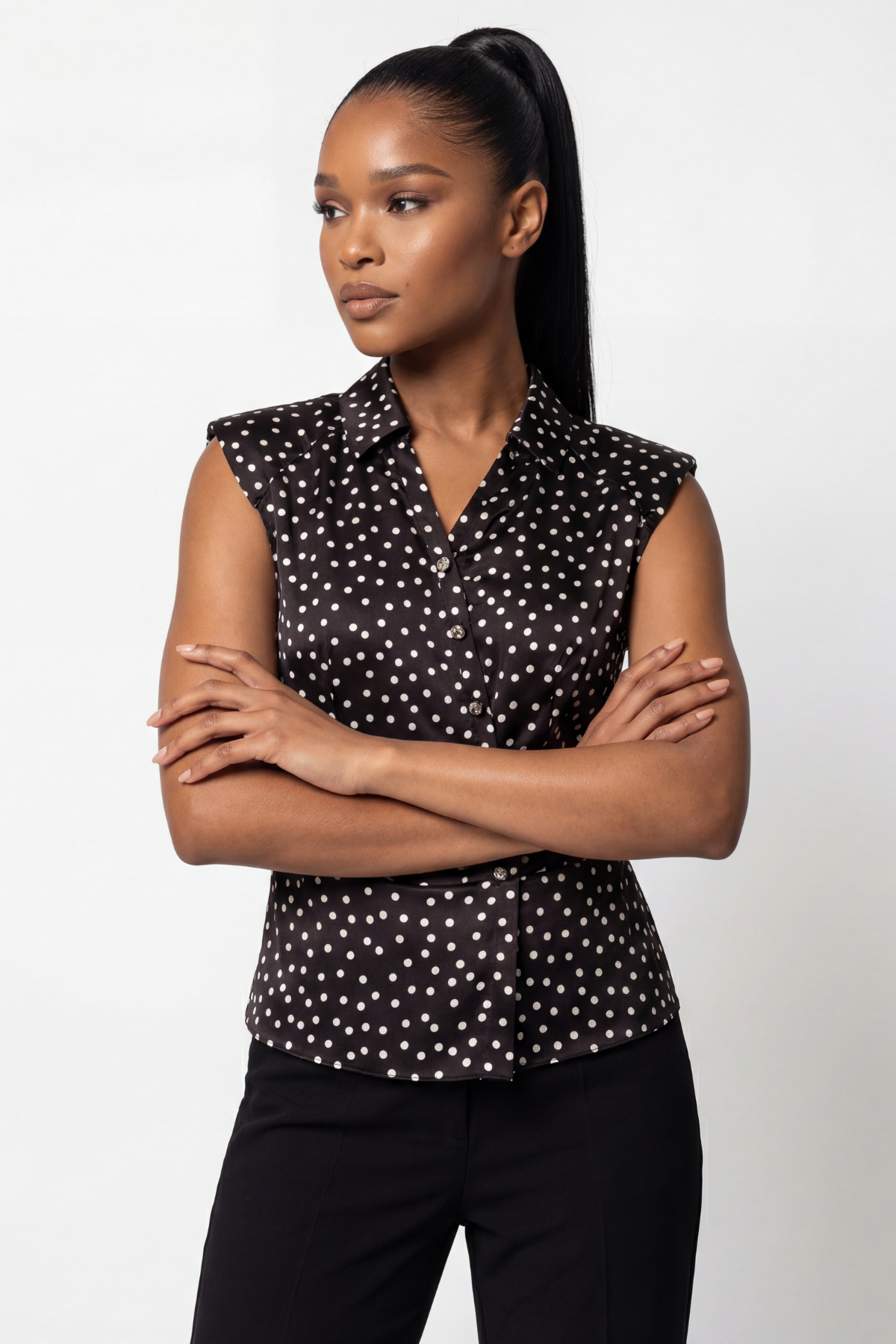 Woman wearing a black sleeveless top with white polka dots and black pants on a white background
