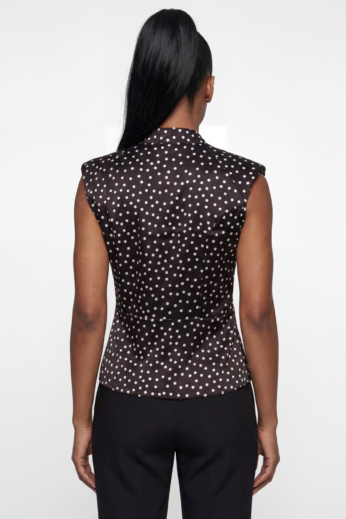 Woman wearing a black sleeveless top with white polka dots on a white background