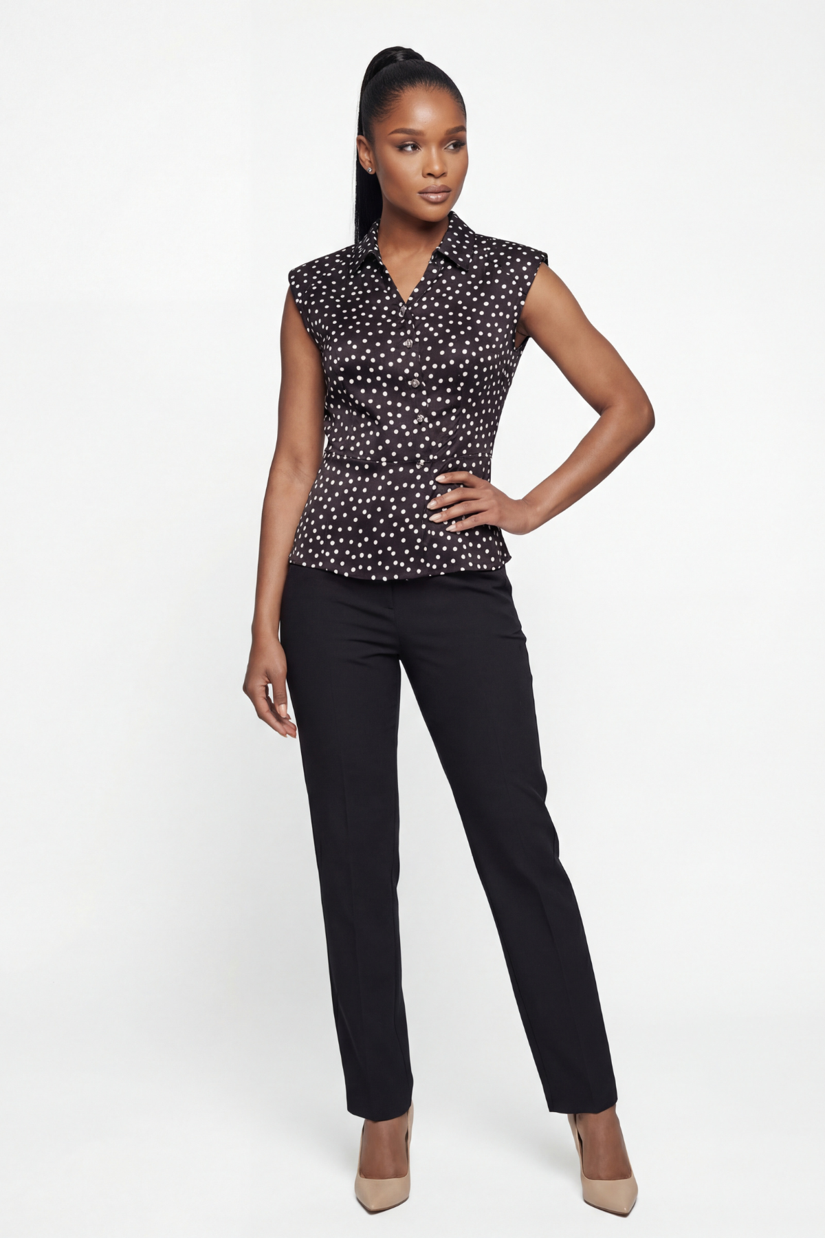 Woman wearing a black and white patterned sleeveless blouse with black pants on a white background