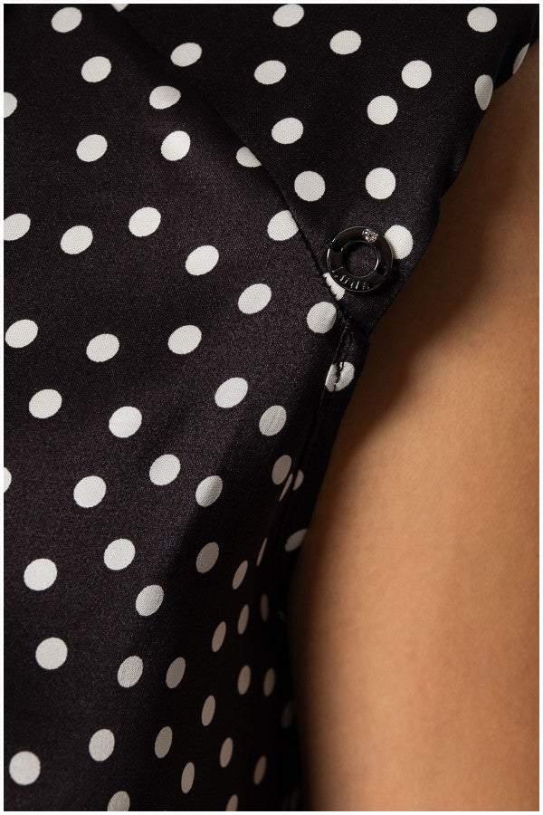 Close-up of black satin sleeveless elegant blouse with white polka dots and decorative diagonal button detail