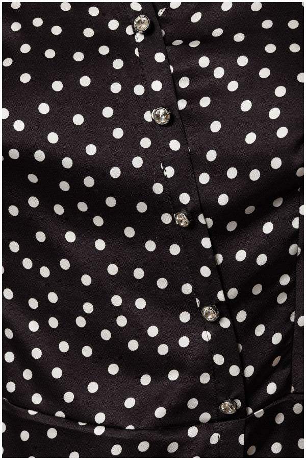 Close-up of black satin elegant blouse with white polka dots and decorative diagonal buttons on smooth fabric.