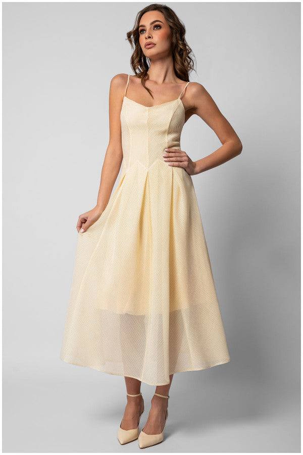 Woman wearing an elegant midi dress in ivory with thin straps and a flowing A-line silhouette standing against gray background