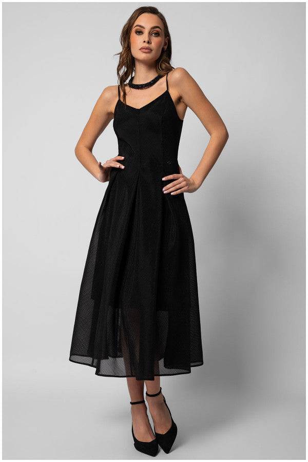 Woman wearing a black elegant midi dress with a fitted bodice, A-line silhouette, delicate straps, and black heels against a gray background