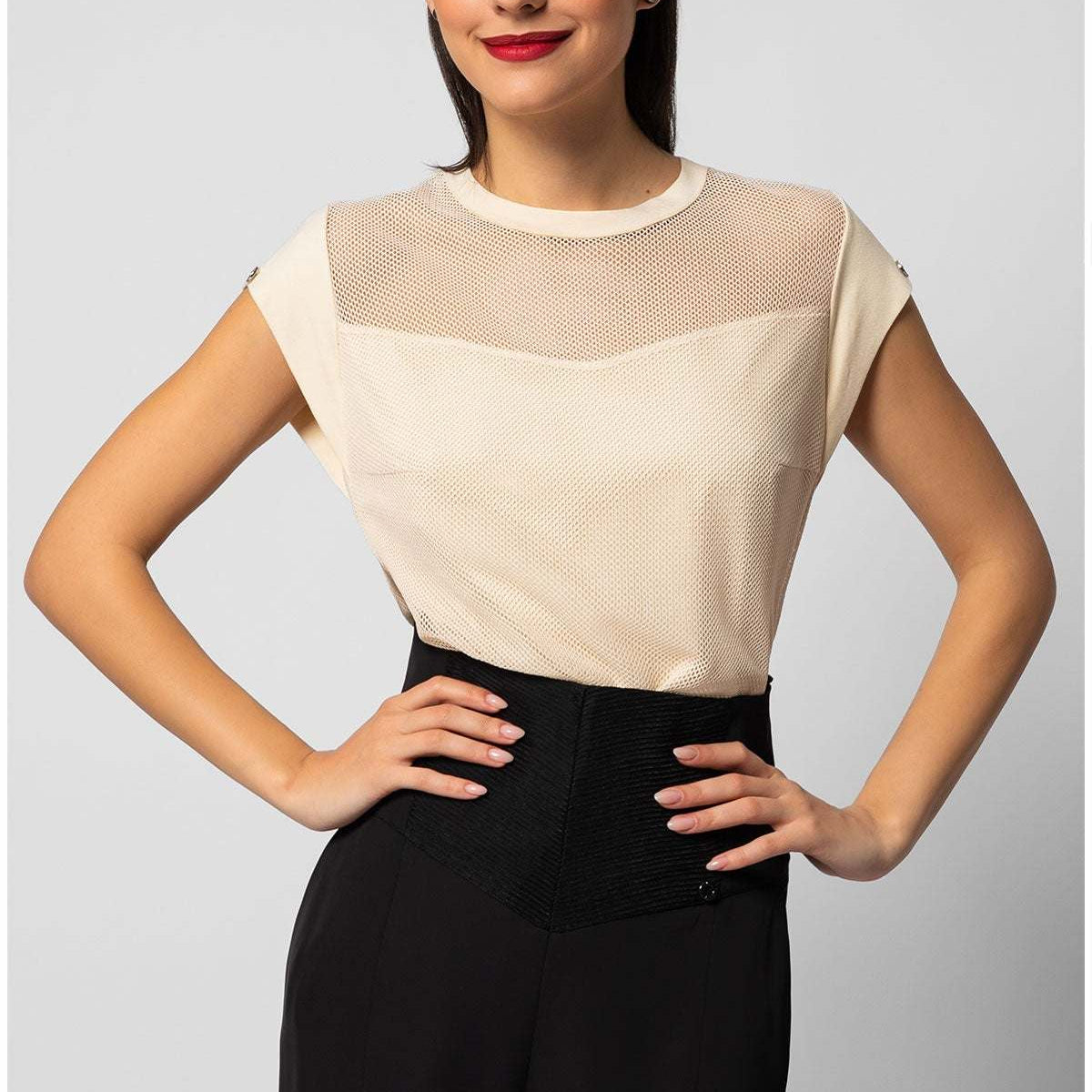 Woman wearing a cream womens short sleeve blouse with sheer paneling at the neckline paired with black pants