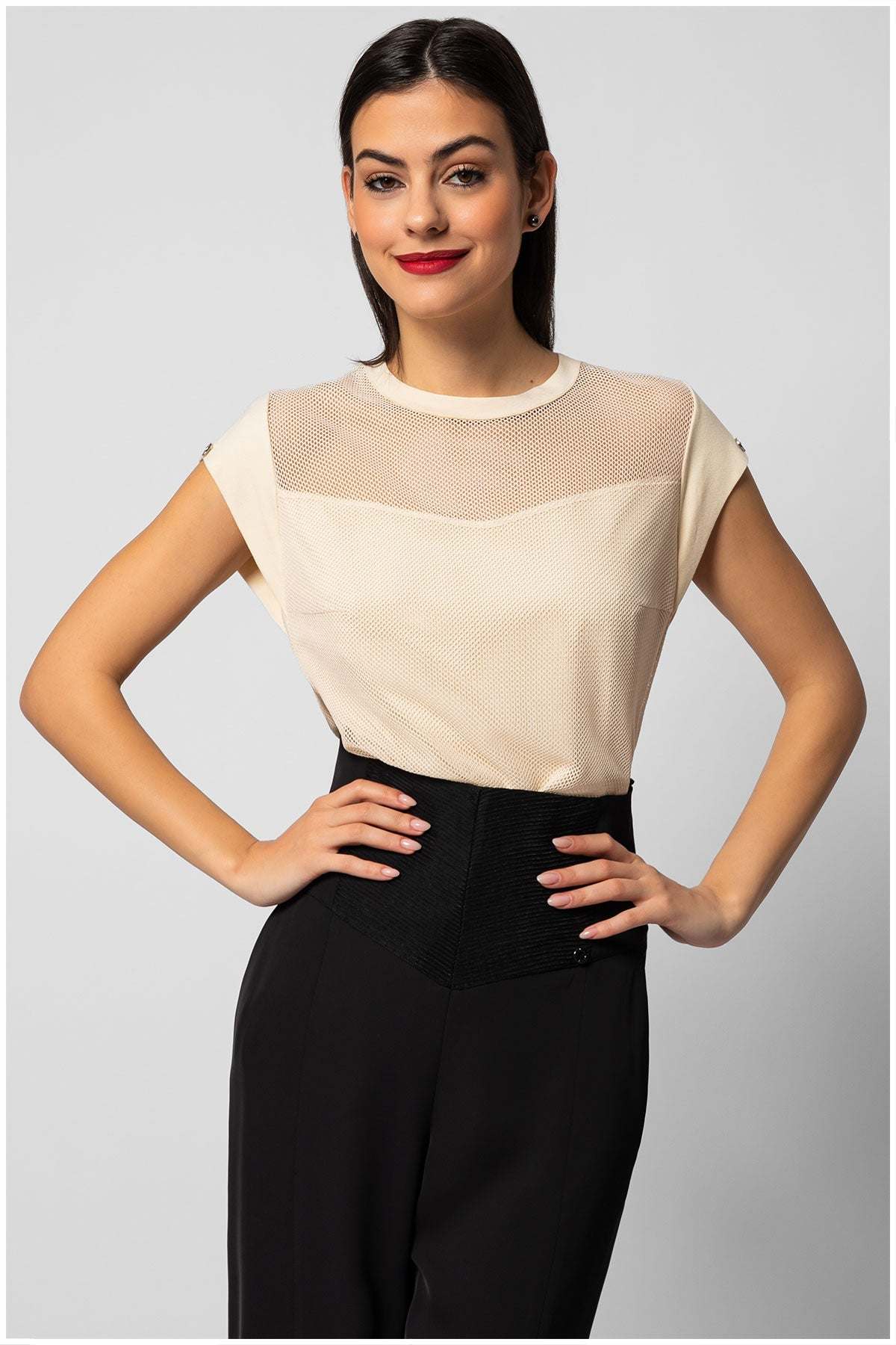 Woman wearing a cream womens short sleeve blouse with sheer paneling at the neckline paired with black pants