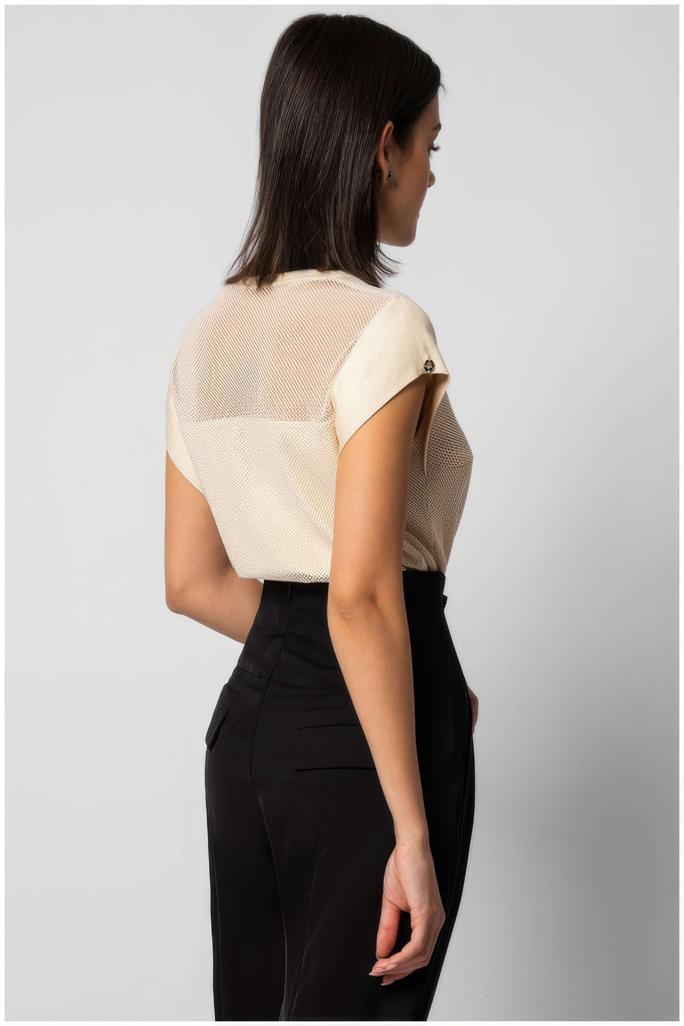 Woman wearing Aria Short-Sleeve Blouse in Ivory with delicate mesh back and tailored fit paired with black pants