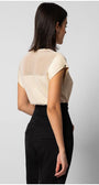 Woman wearing cream short sleeve blouse with sheer panel and black trousers standing sideways against gray background womens short sleeve tops
