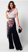 Woman wearing floral Overall with navy flared trousers and a belted waist, holding a small handbag.