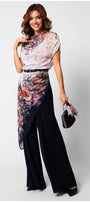 Woman wearing floral Overall with navy flared trousers and a belted waist, holding a small handbag.