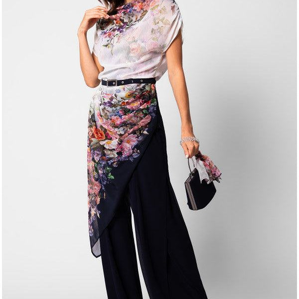 Woman wearing floral Overall with navy flared trousers and a belted waist, holding a small handbag.