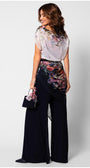 Woman wearing the floral-overall-tina-two-layer with floral top and navy flared trousers, holding a matching handbag.